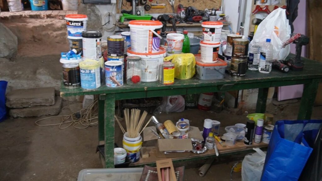 Farbe, lakovi i alat privremeno odloženi na sto pre sortiranja i organizacije u radionici.