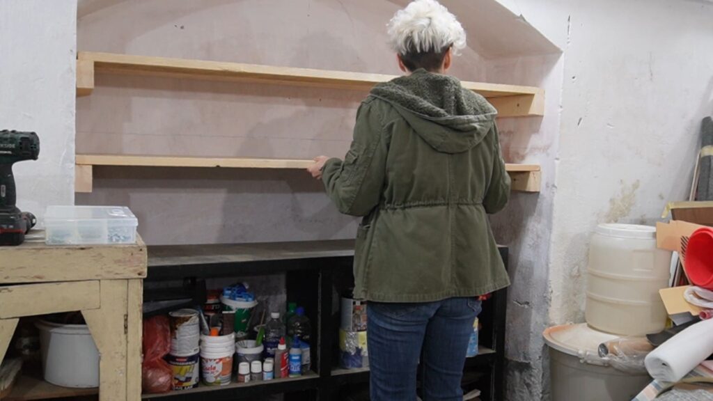 Postavljanje završne daske na nosače tokom montaže police u radionici.