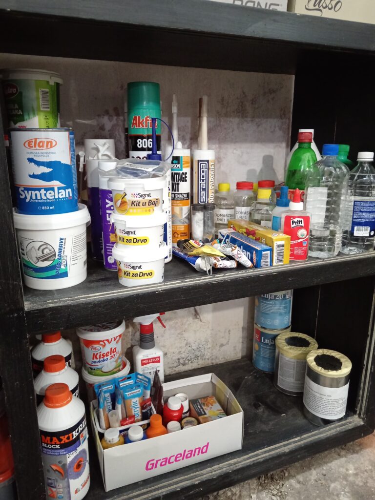 Lepkovi, gitovi, prajmeri i razređivači organizovani na polici po vrsti materijala.