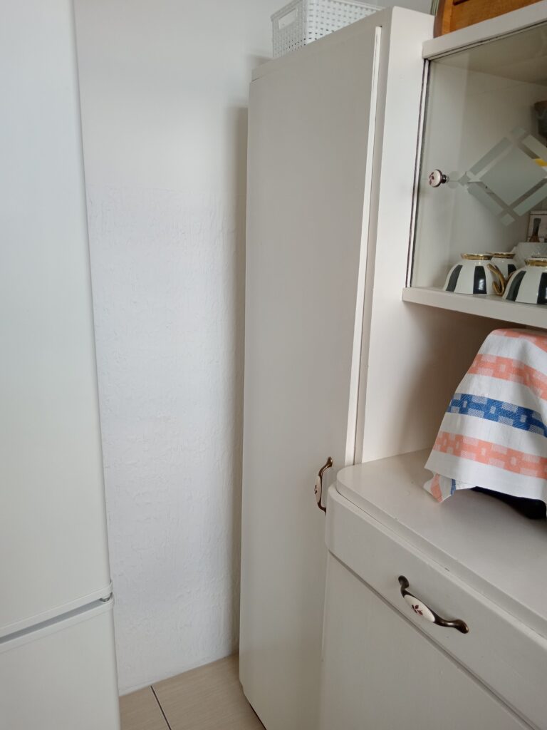 Prazan uzan prostor između zida i belog kuhinjskog kredenca.