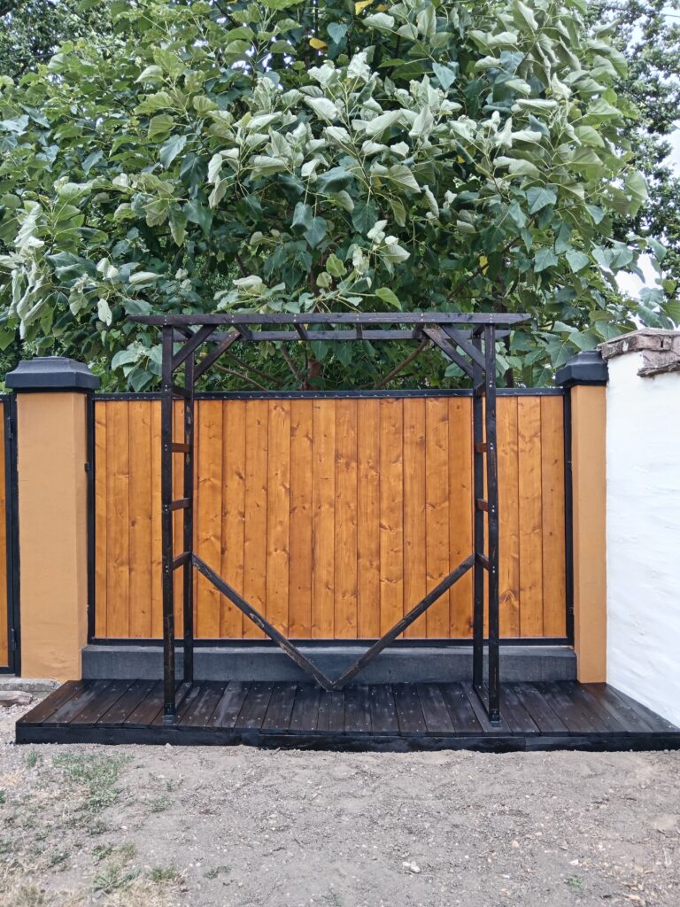 Mini pergola sa dijagonalnim kosnicima pričvršćena na drvenu platformu uz ogradu